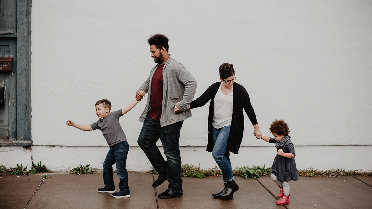 A family of four, with a little boy and little girl, walk hand in hand.