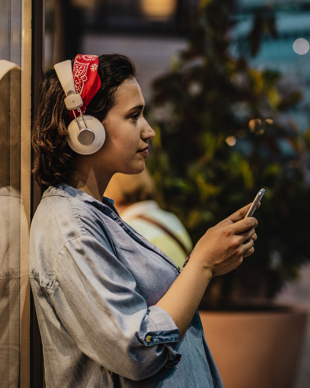 A woman in a red bandana listens to a podcast on a sidewalk in evening